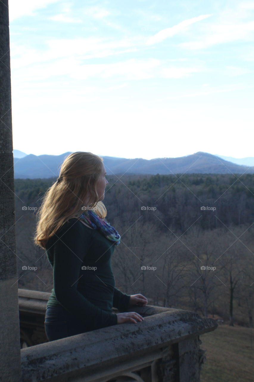 Blonde girl looking out on a balcony overseeing beautiful mountain range