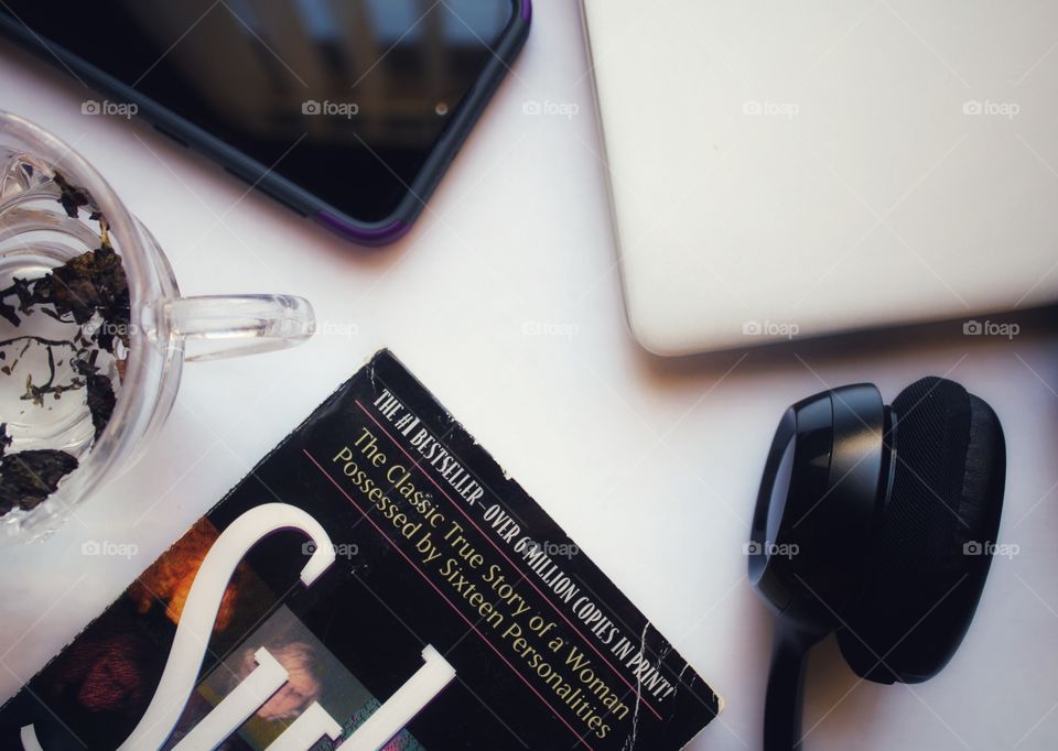 a cup of tea, mobile phone, book, laptop and headphones for lazy weekend