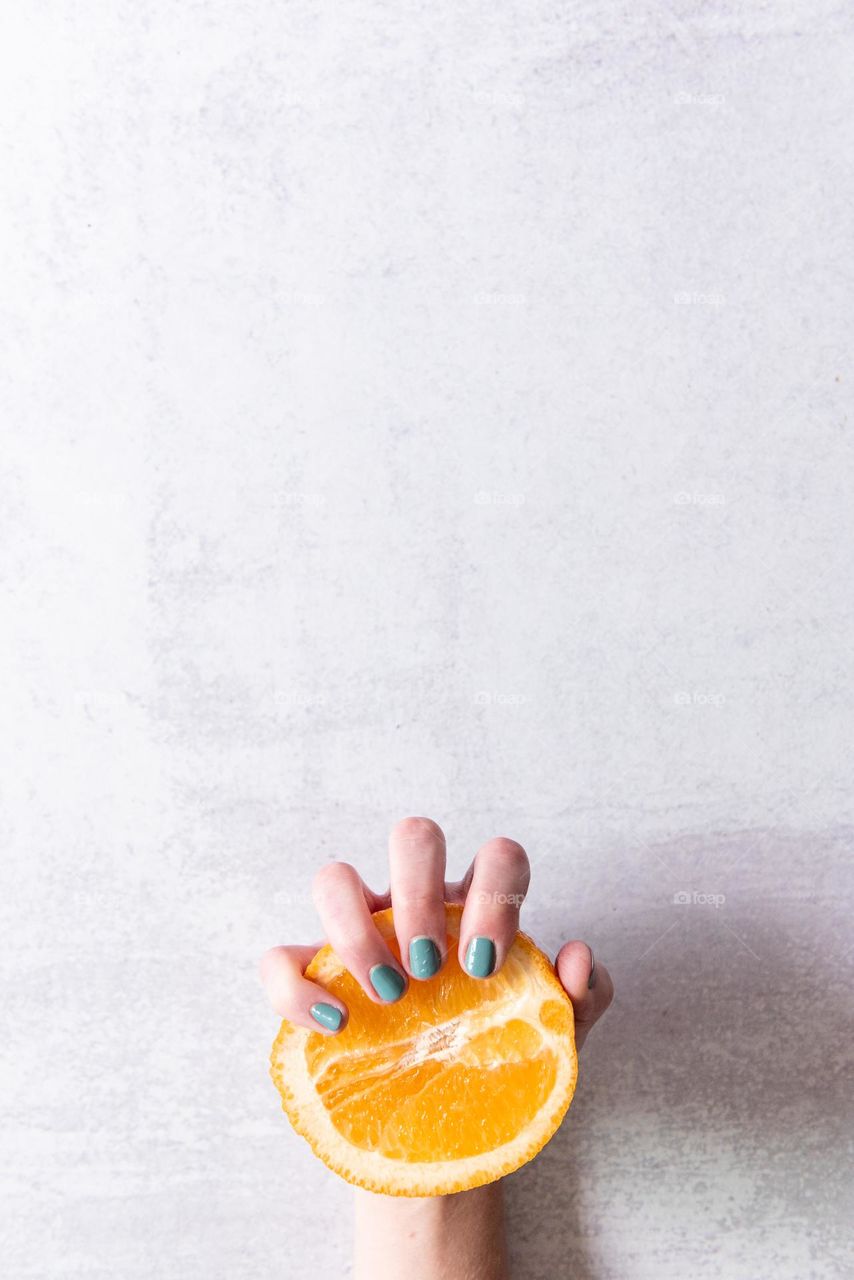 Woman’s hand with painted nails holding half of an orange fruit