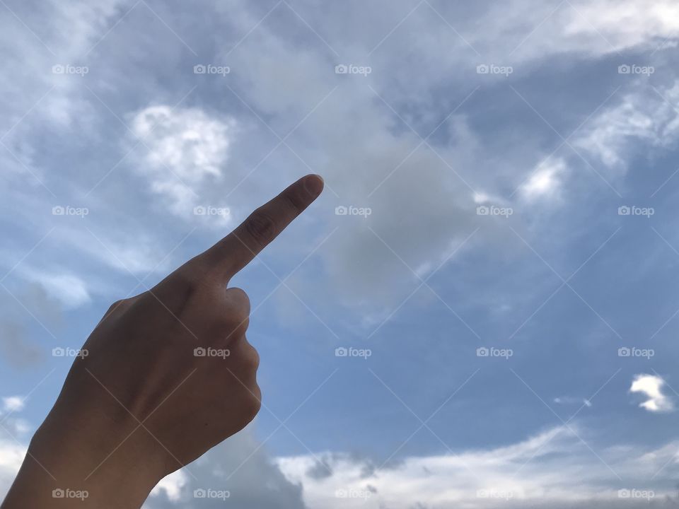 woman uses her right forefinger pointing up in the bright blue sky with white cloud in daylight with copy space on the right side of frame
