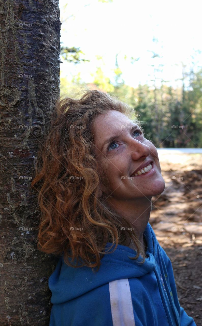 Portrait of a woman leaning against a tree looking up.