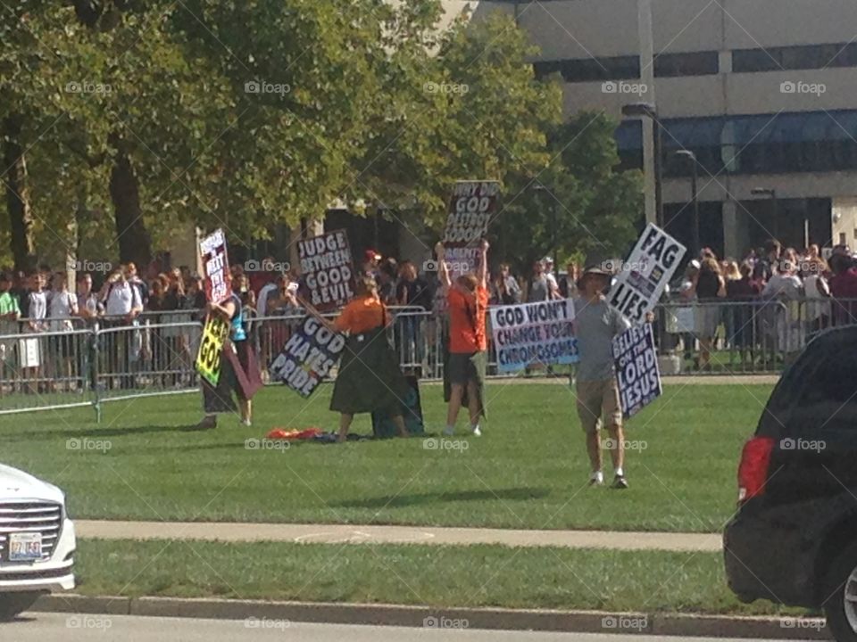 Westboro Baptist church members holding signs to protest an LGB club formed by students of IUPUI.  Club supporters and spectators stand in the background behind the fence.