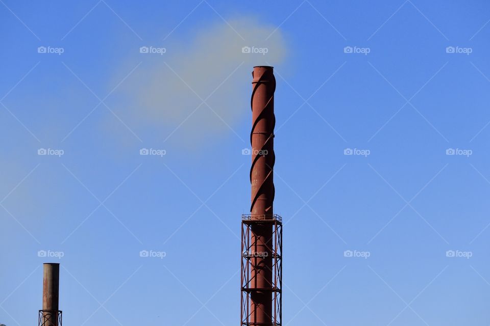 Rusted iron ore steel making industry tower chimney stack blowing plume of smoke into vivid clear blue sky 