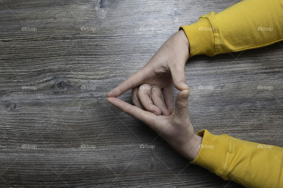 Men's hands in a yellow jacket lie on a gray wooden surface, which is used as a background or a surface with incident light.