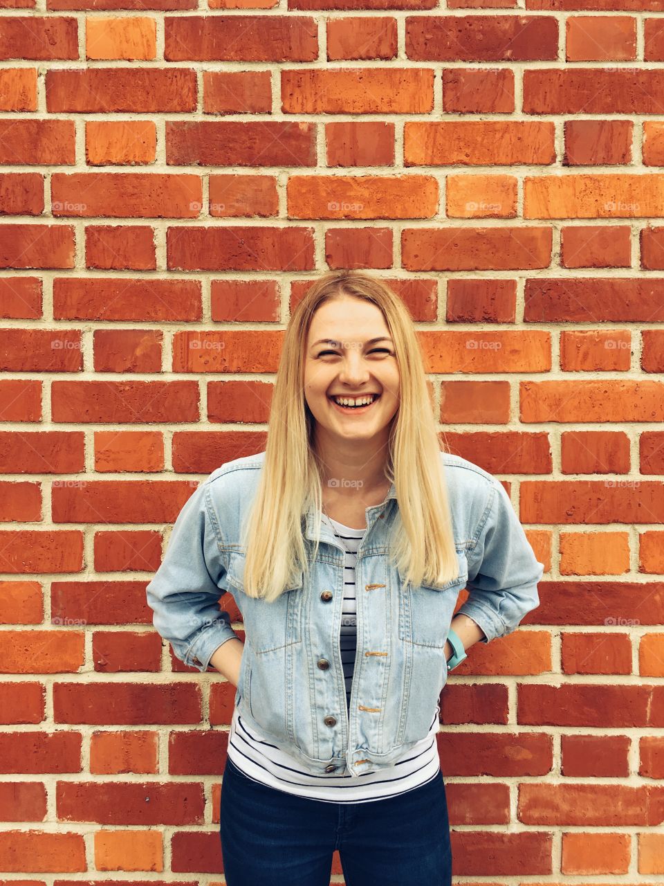 Young blonde girl smiling near brick wall.