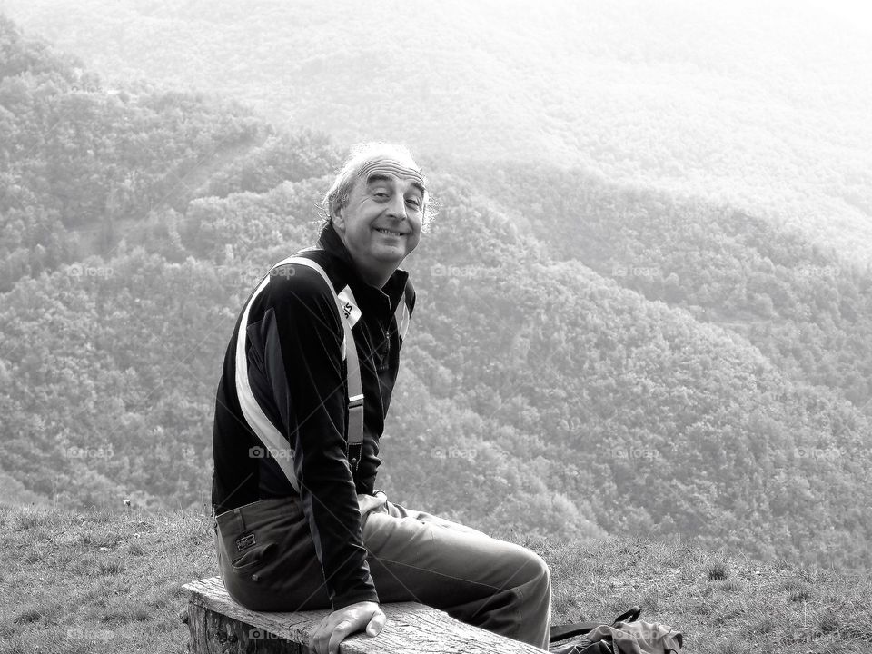 Man smiling sitting on top of mountains in Tuscany, Italy