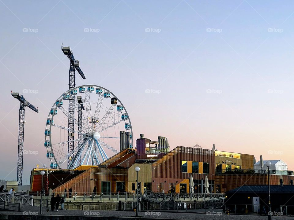 Cityscape Helsinki view to the ferris sky wheel, two cranes and the restaurant sauna Allas against the gentle sunset sky