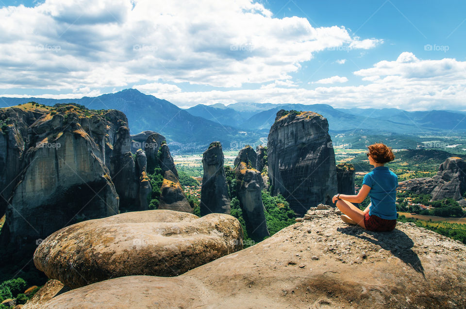 Young woman sits back to the camera on top of the mount and looks at the valley and rocks, Meteora, Greece