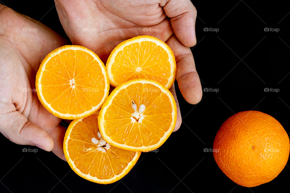 The slice of fresh orange in the hand on dark background. Top view. Concept of healthy lifestyle.