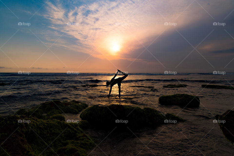 Silhouette of an anonymous man doing yoga pose on the beautiful beach during sunset hours