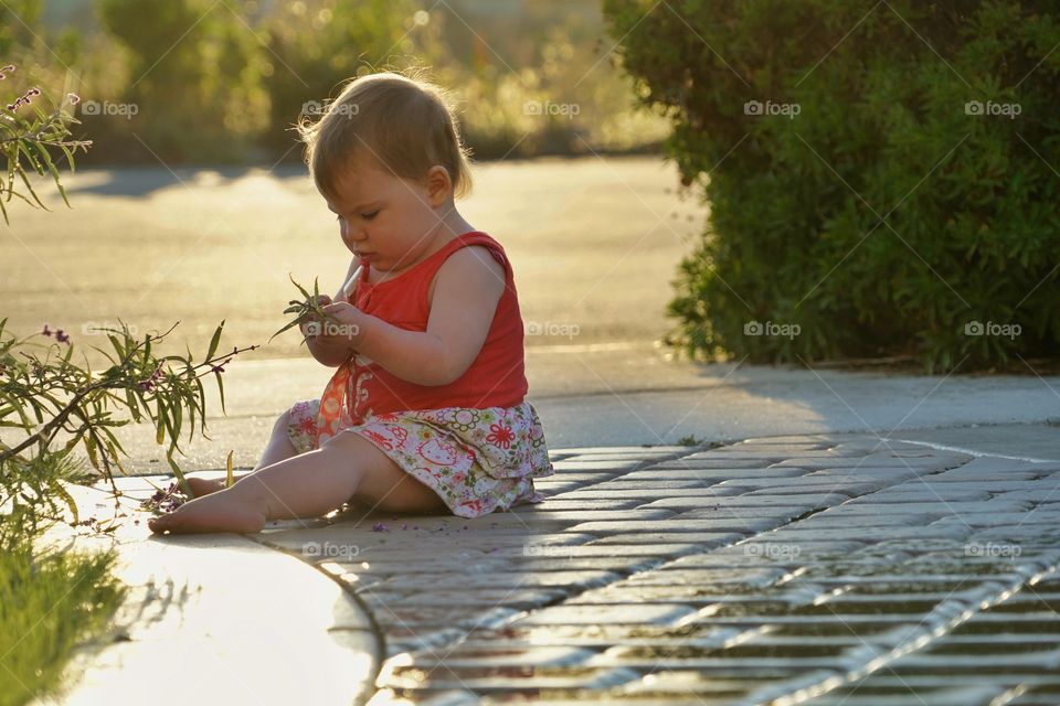 Toddler Girl Sitting On Wet Tiles Outside During Golden Hour