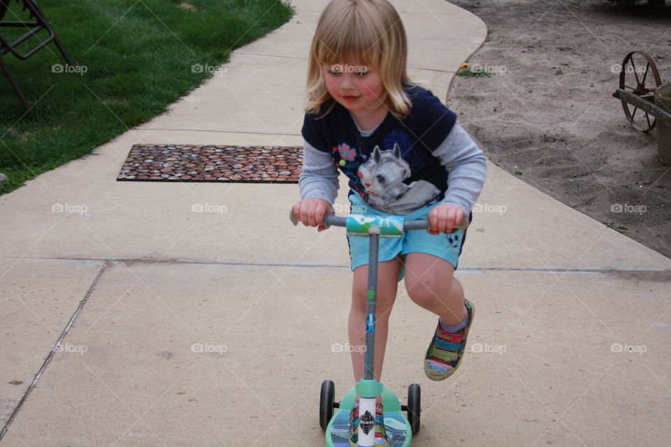 Happy little girl riding a scooter