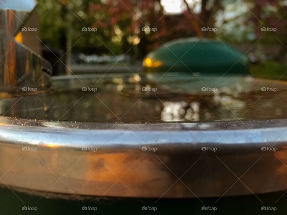 Full drinking fountain at park. Reflections of trees in water of filled drinking fountain 