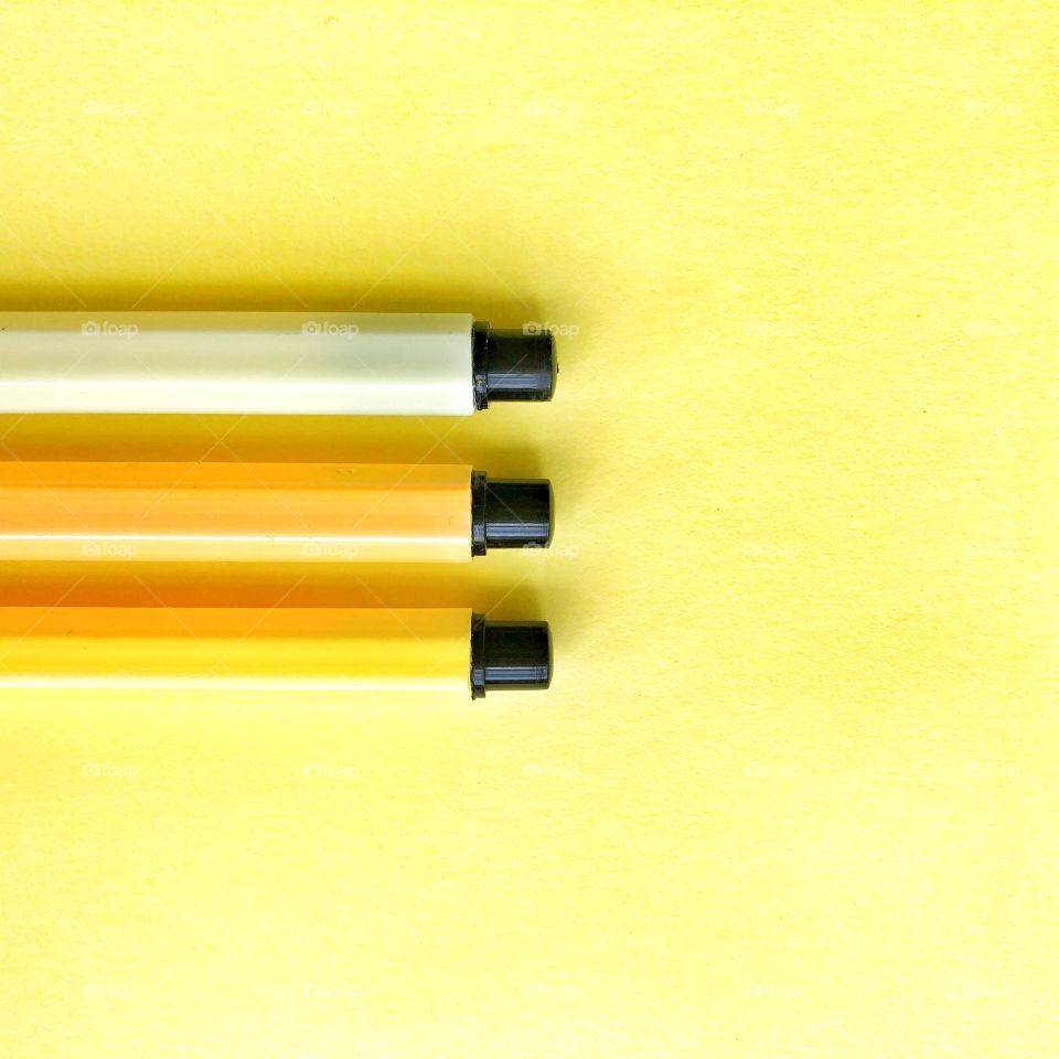 Minimal shot of three shades of yellow pens on yello  background 