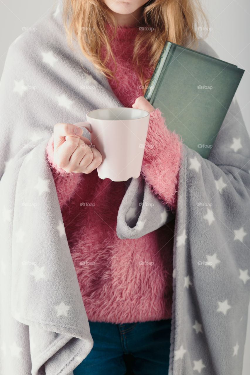 Enjoying the drinking coffee and reading a book. Young girl holding book and cup of coffee going to relax at home