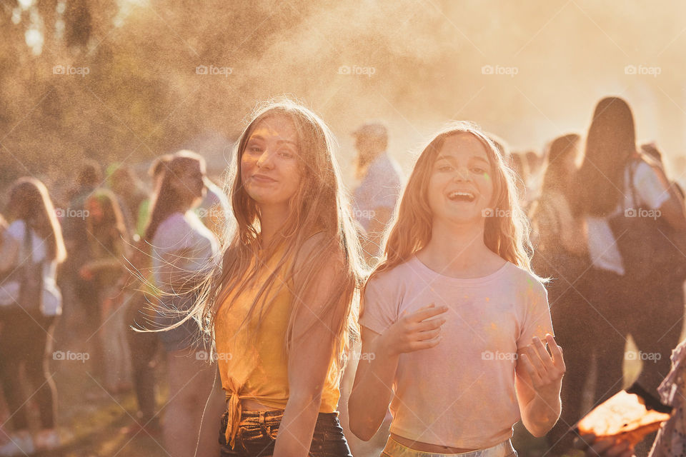 Portrait of happy smiling young girls with colorful paints on faces and clothes. Two friends spending time on holi color festival