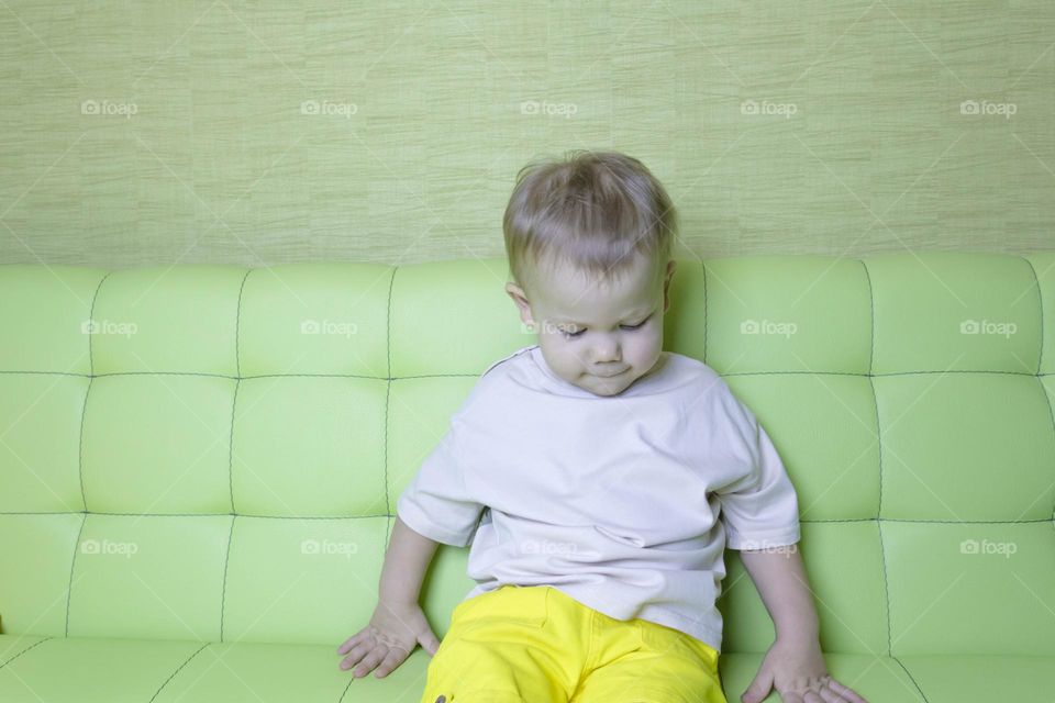 A portrait of a child sitting at home on a green sofa depicts different emotions in yellow shorts.