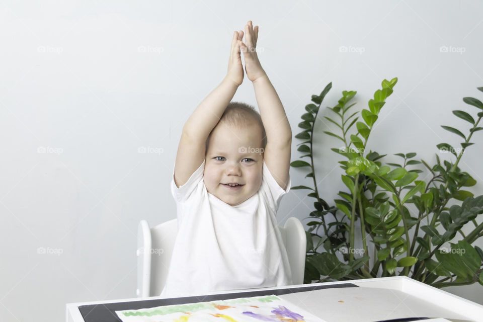 A small child draws with watercolors, multi-colored paints in an album at the table.