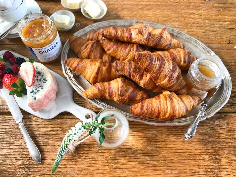 Breakfast with croissants, butter, jam, cheese, strawberries, flower in a vase