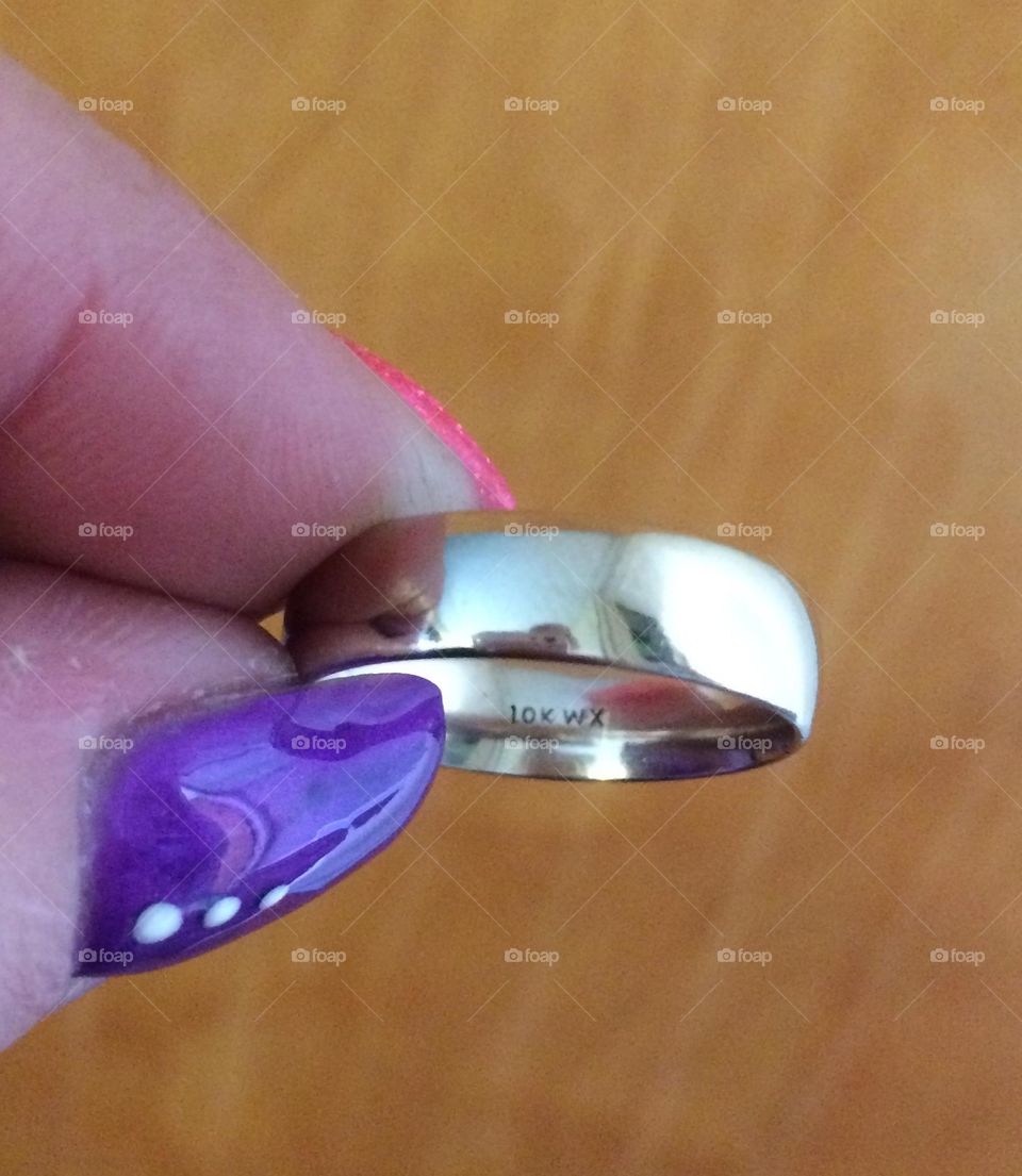 Nicely manicured thumb and pointer finger, long painted fingernails hold a mens gold wedding band thats for sale