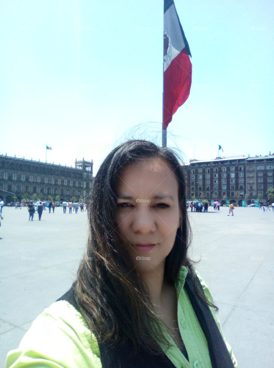 selfie mujer cabello suelto de fondo la bandera de México en el Zócalo de la CDMX con edificios de fondo