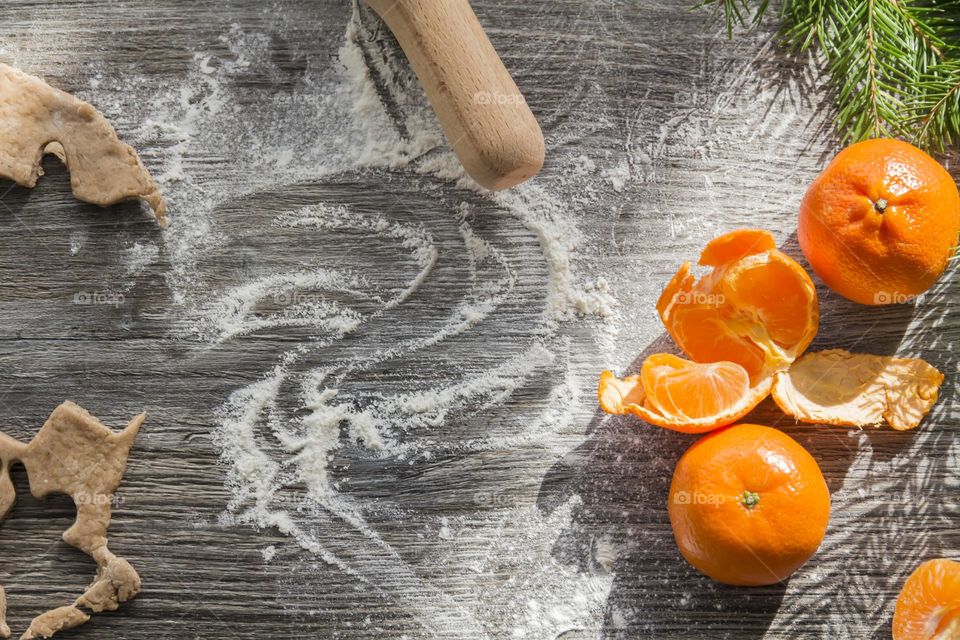 Christmas, gingerbread cookies on a wooden table sprinkled with flour, with tangerines and a green Christmas tree.