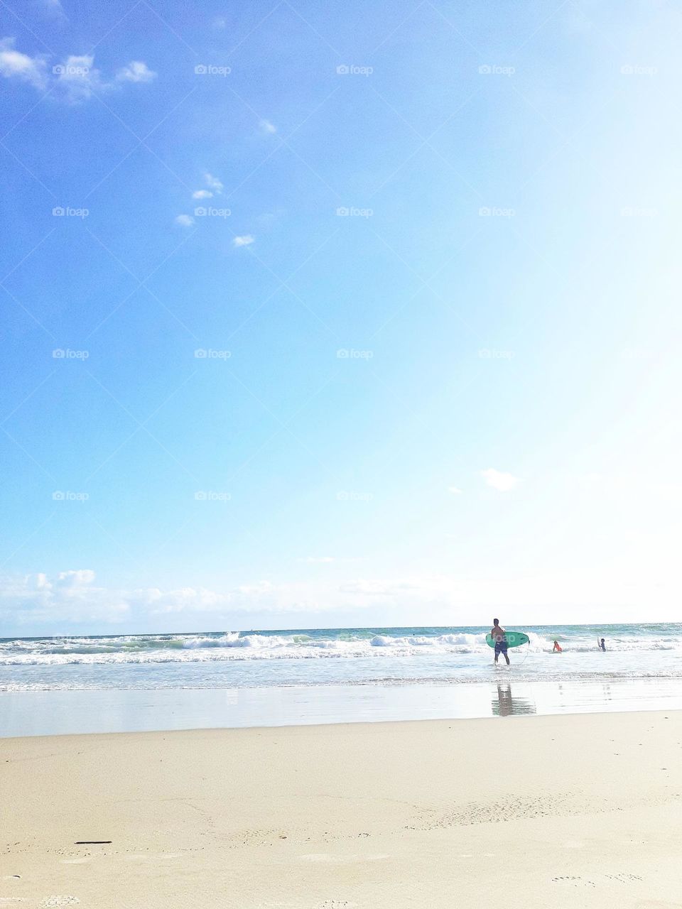 A surfer carries his surfboard into the ocean to surf at Indian Rocks Beach in Tampa, Florida.