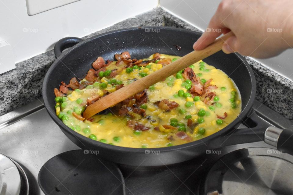 Homecooking cooking Frittata at home and adding and mixing ingredients and removing the Frittata from the pan for cutting and serving on a white plate with tomatoes. Healthy home cooking in kitchen. Breakfast and lunch food preparation. 