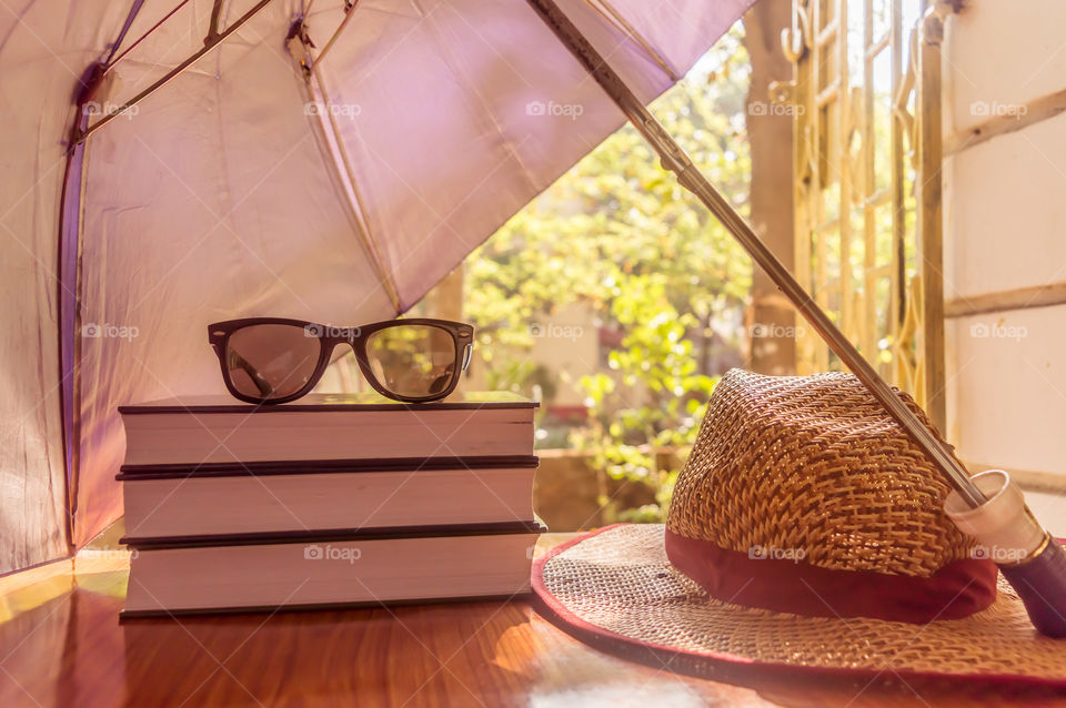 Sunburn risk concept protect your skin from temperatures, Umbrella protecting beautiful woman things. Books sunglasses and a straw hat. Summer holiday concept with copy space room for text.