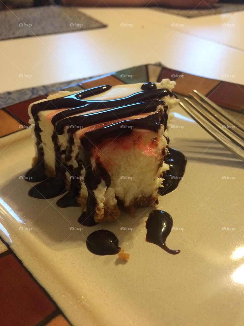 Food, dessert photo, with a plated piece of delicious, homemade, cherry cheesecake on a graham wafer pie shell, with dark chocolate sauce drizzled on top, with the metal fork that took a bite out of it