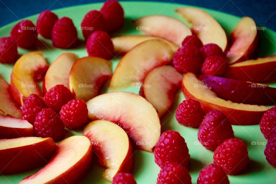 Decorative arrangement of fresh nectarine slices and raspberries on a green plate with green background 