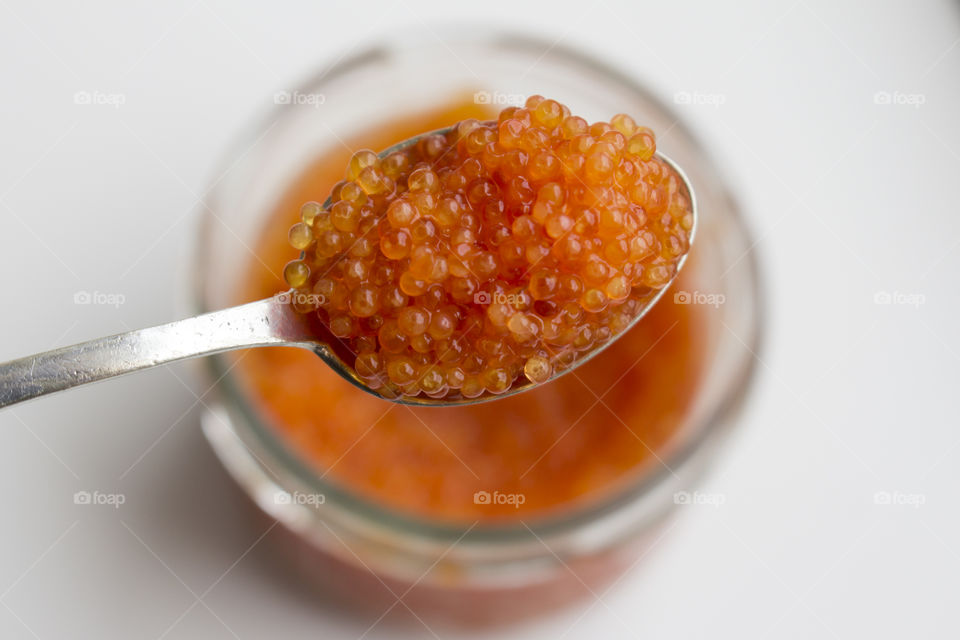 Orange caviar on a spoon above a glass jar 