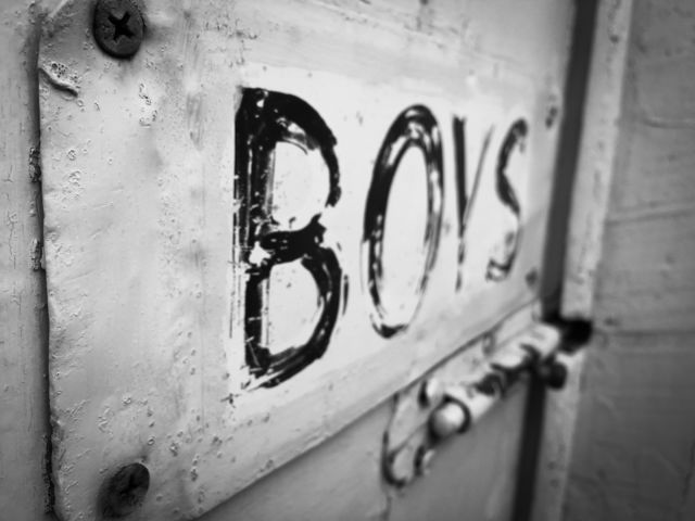 Black and white photo, rusty old door with old painted tin sign which reads BOYS. Old outside toilet, outside John, outside loo, men's room, boys room, 