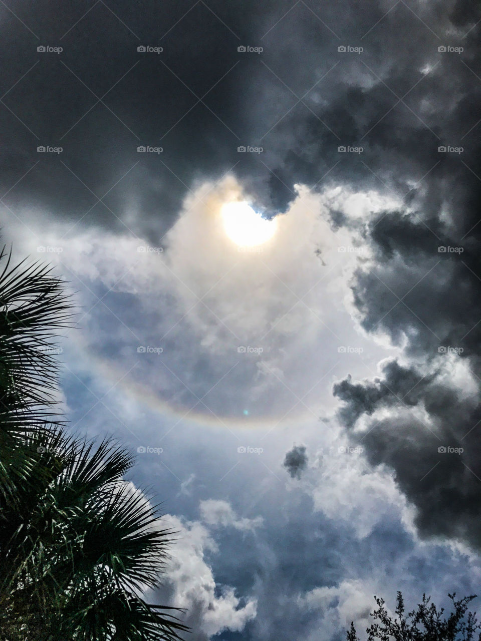 Stormy clouds closing in around sun ring and blue sky