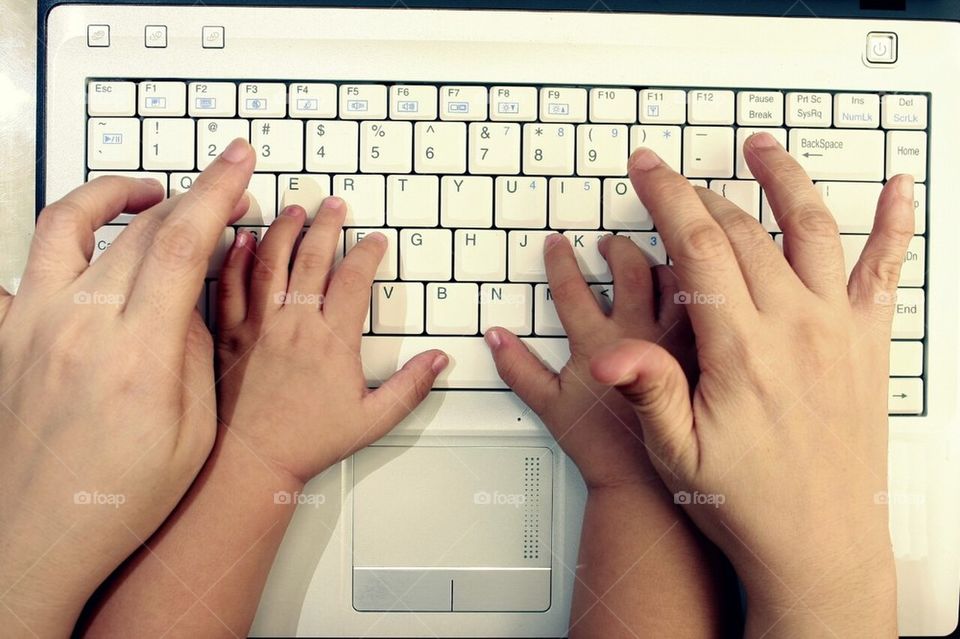 Hands of an adult guiding or teaching a child's hand to type on a