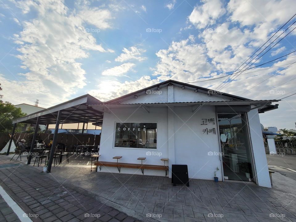 A day of good weather, blue sky and white clouds, white building, a cafe with outdoor seating