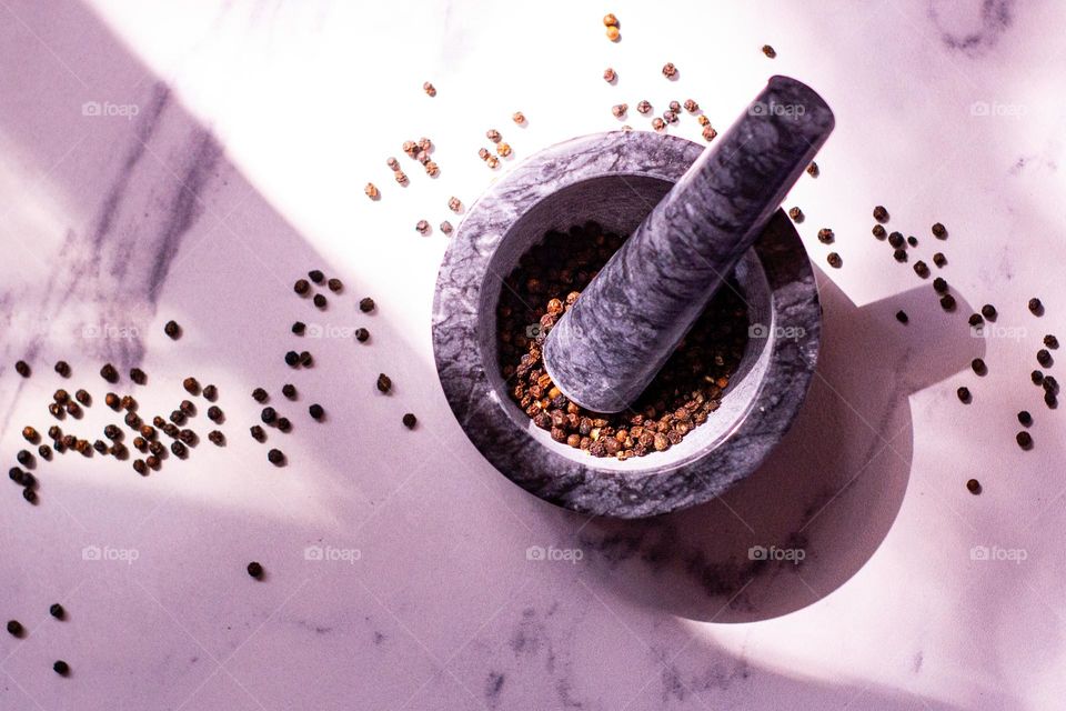 Whole black peppercorns in a Marble mortar  on a marble countertop.