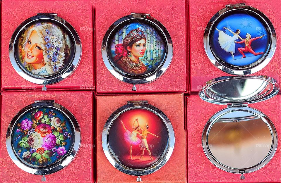 Circles. There are six round mirrors on the red boxes. One mirror is open. On the surface of five mirrors are various images of hand-made technique with enamel