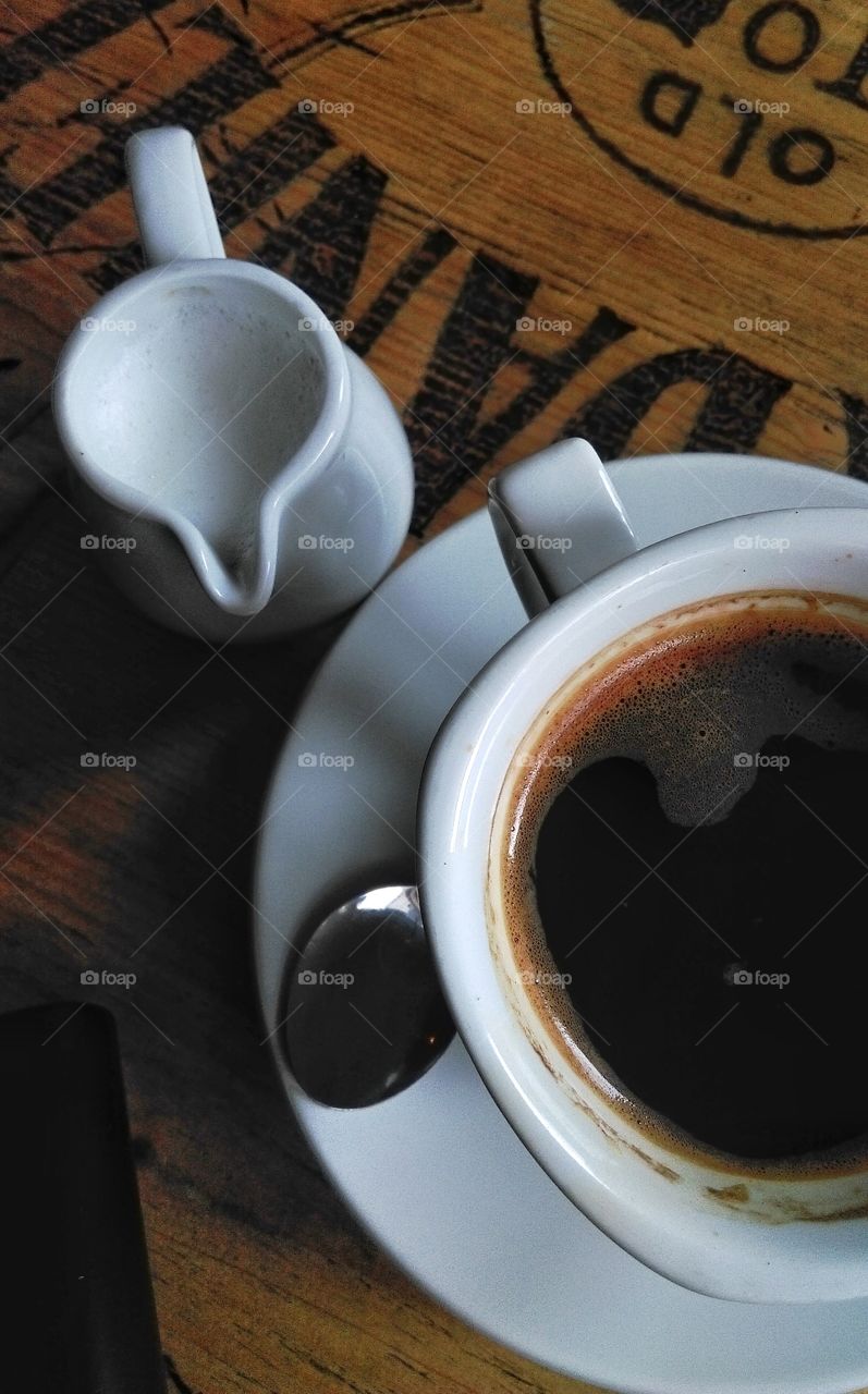 Cup of coffee with milk jug on wooden table