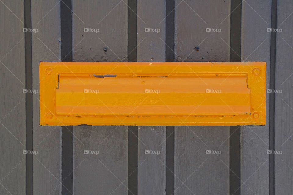 An orange private mail slot on a wooden industrial fence in New York City.
