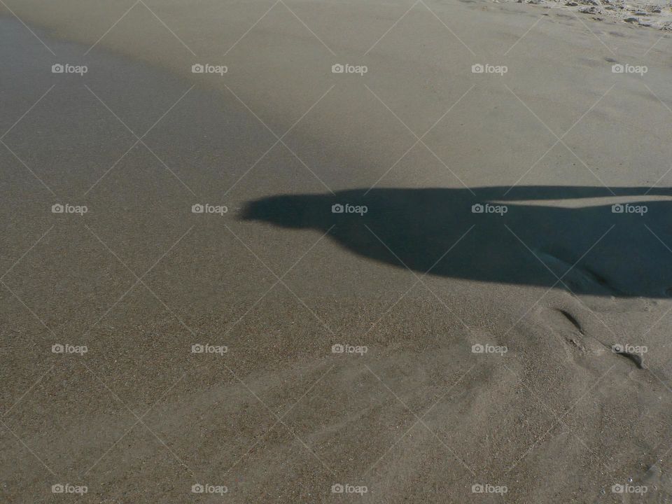 Shadow of one person woman walking on the seashore at the beach on the wet sand from the ocean waves in the evening with sunset.