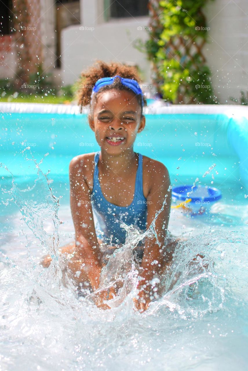 Cute little girl enjoying some playtime in a swimming pool during a hot summer day, looking for refreshment