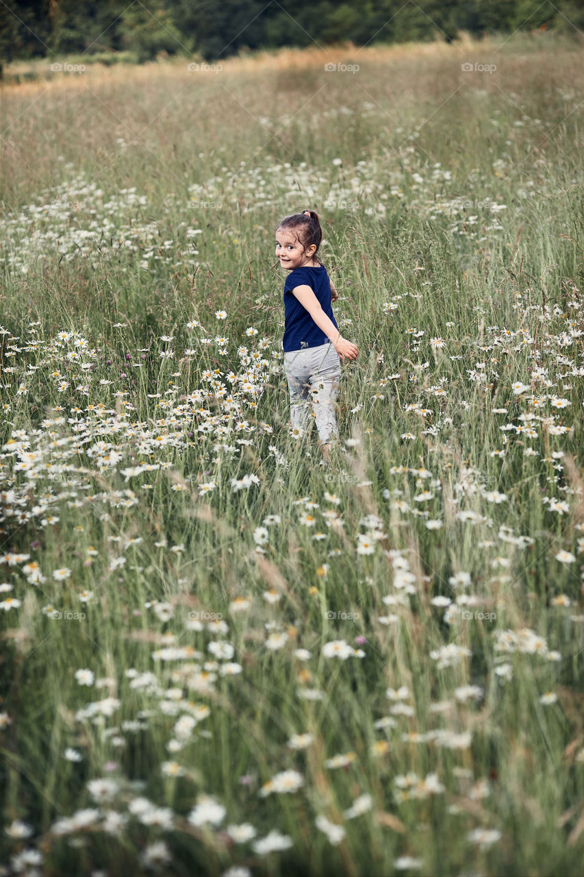 Little happy girl playing in a tall grass in the countryside. Candid people, real moments, authentic situations