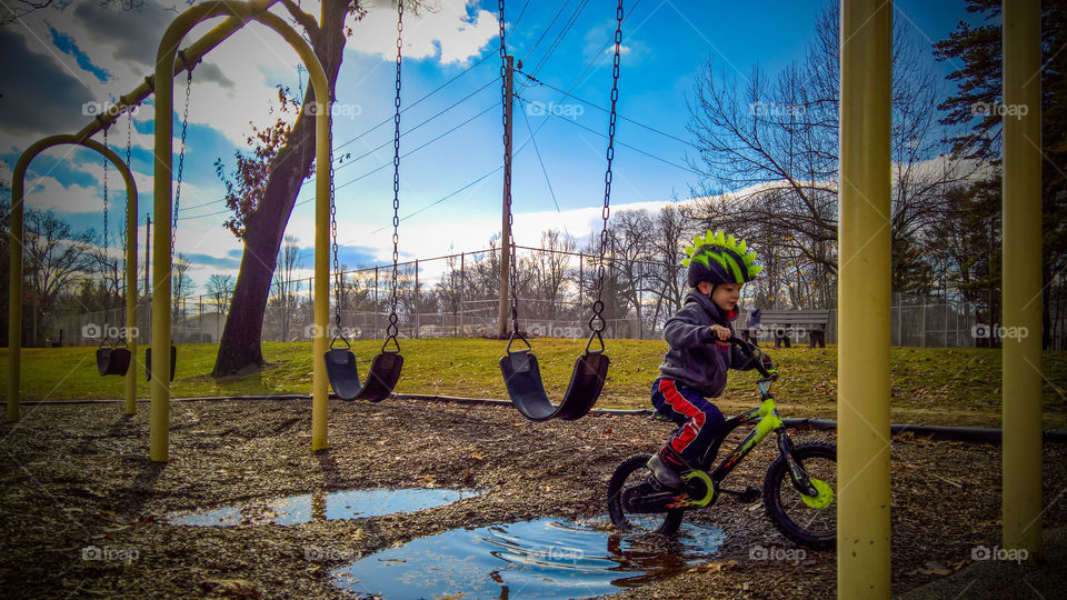 Boy riding bicycle park sunny day swings puddles blue skies