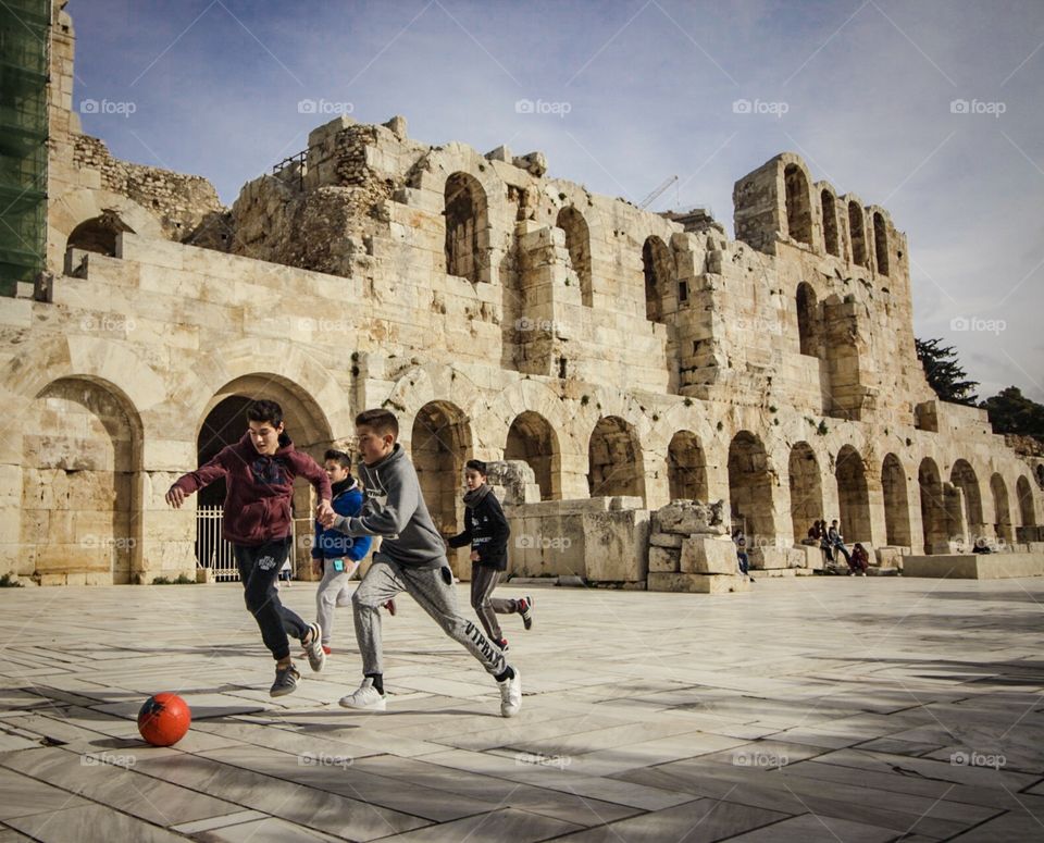 Greek children playing football in front of Ancient Greek Ruins 