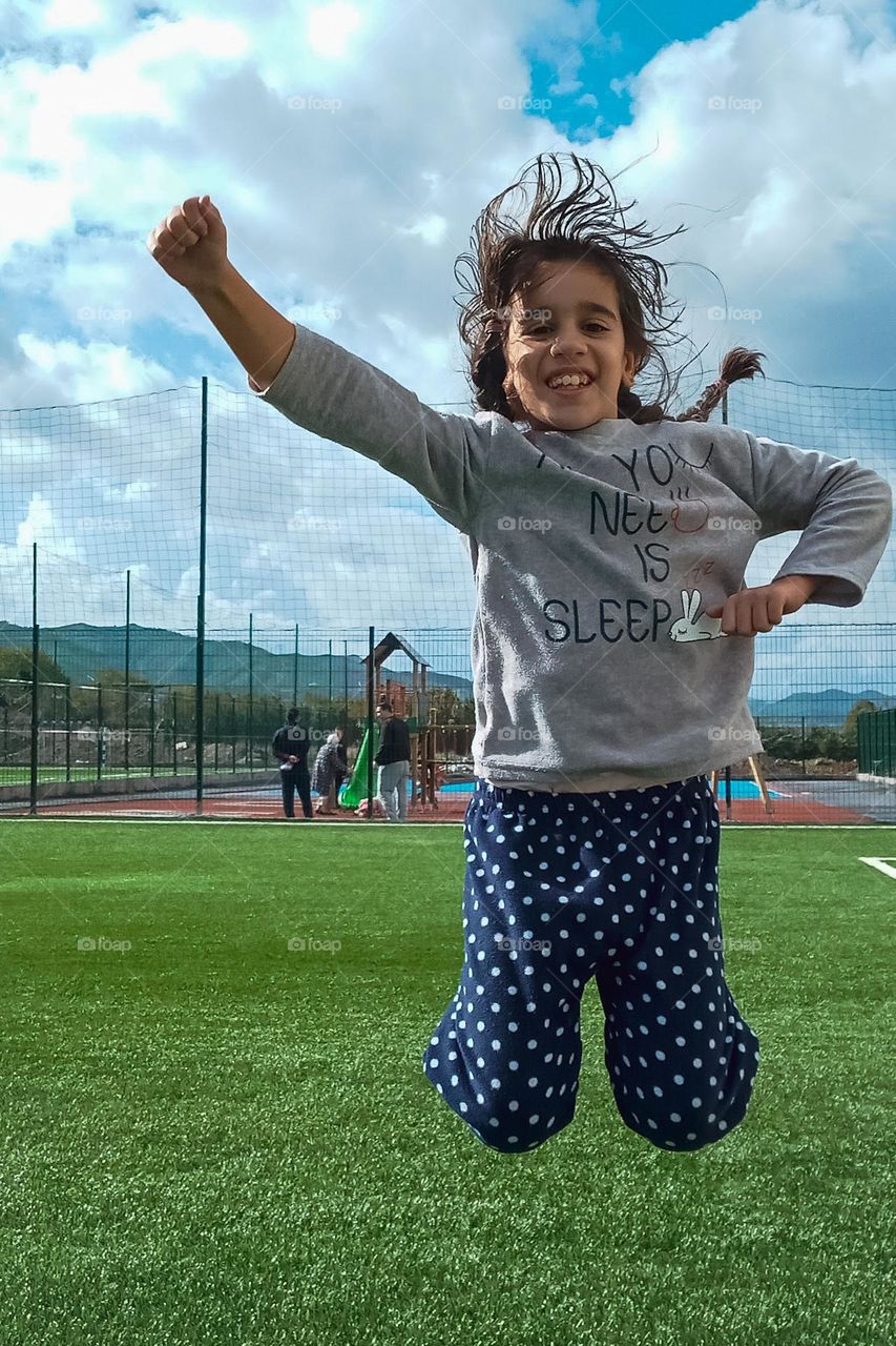 a young girl jumping on a green area