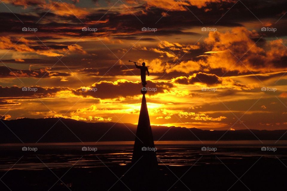 The Angel Moroni Statue atop the Bountiful LDS Temple in Bountiful Utah with against a firey sunset through the clouds
