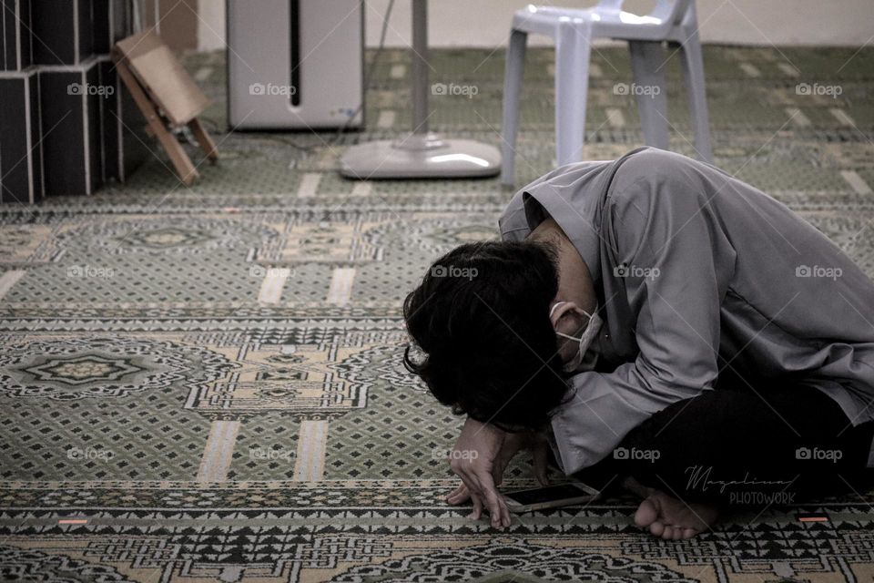 A man sitting alone at a corner of mosque covering his face