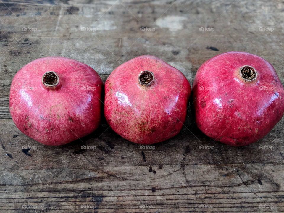 3 red pomegranates on a wooden table