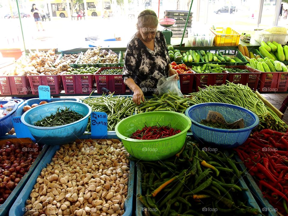 a lady buying fruits and vegetables at a market